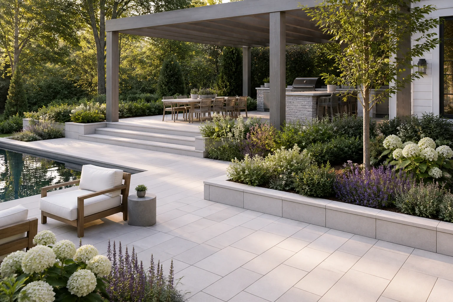 Elegant white-paver garden terrace with pool, pergola, outdoor kitchen, and flowering borders